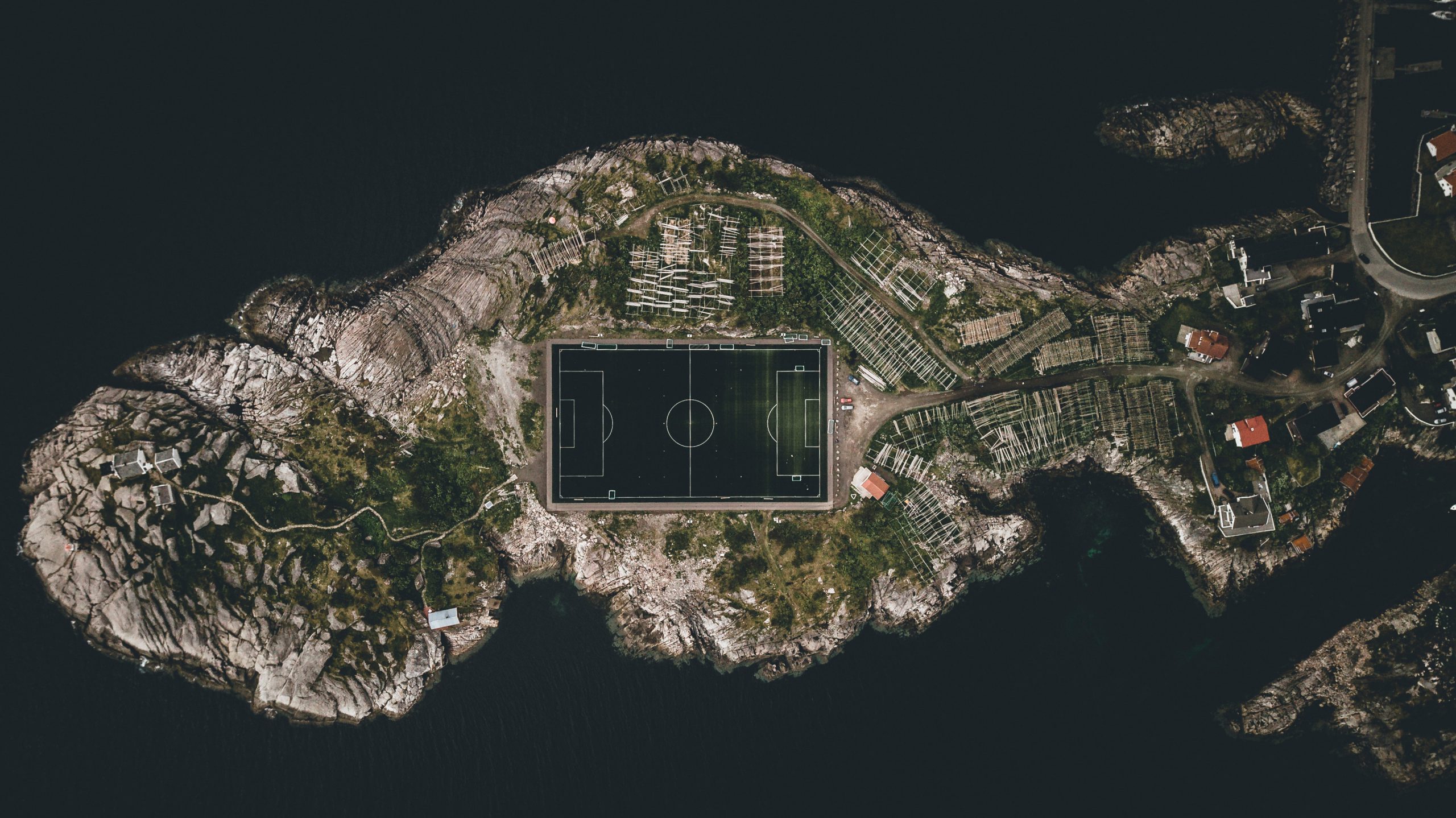 A top-view of a football pitch on a remote headland surrounded by cliffs and the sea